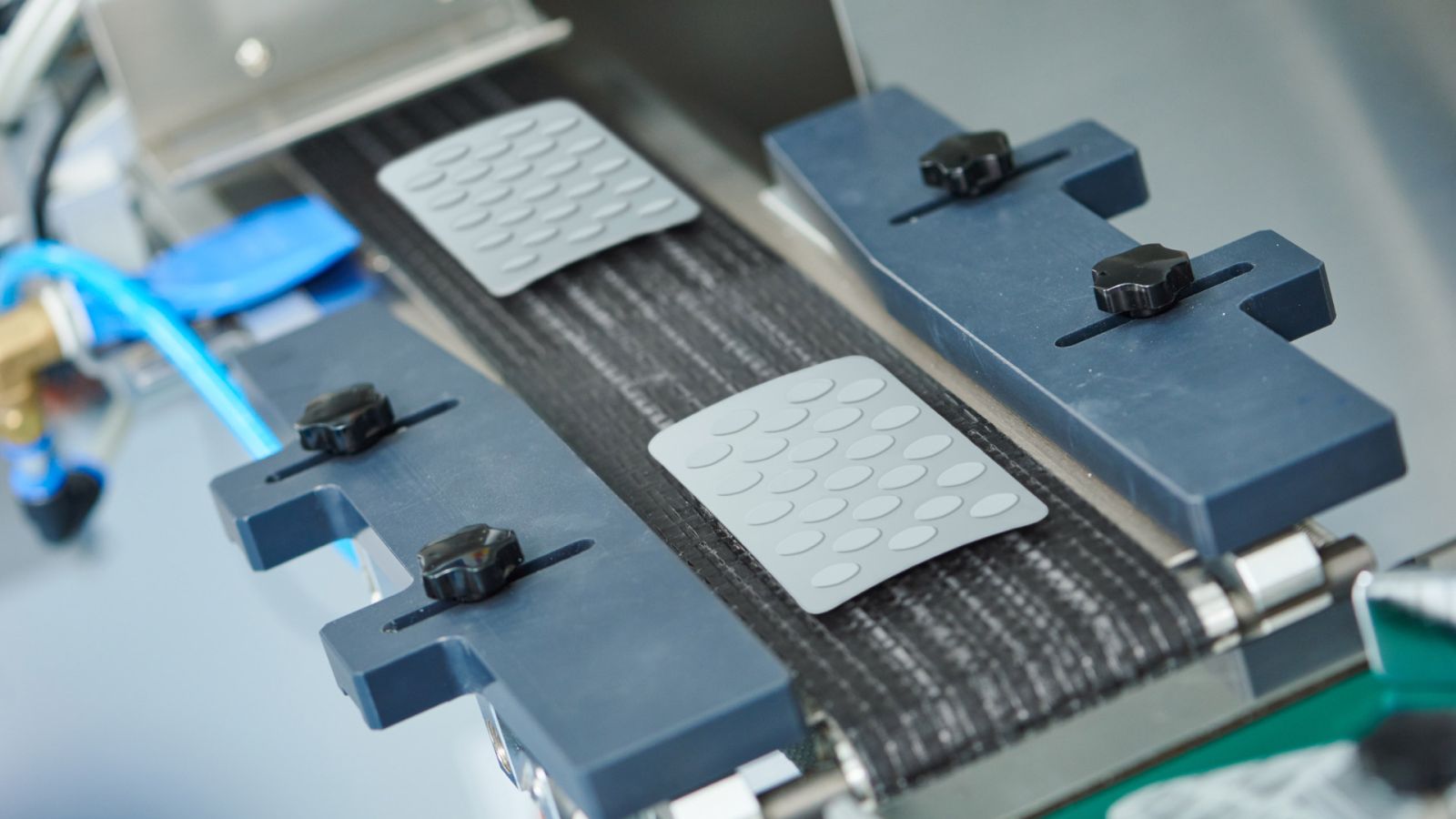 Blister packs with tablets on a conveyor belt in a modern pharmaceutical production line. Focus on precise positioning and inspection mechanisms for maximum GMP compliance and reliable release testing - a key element for safe pharmaceutical production in accordance with regulatory standards.