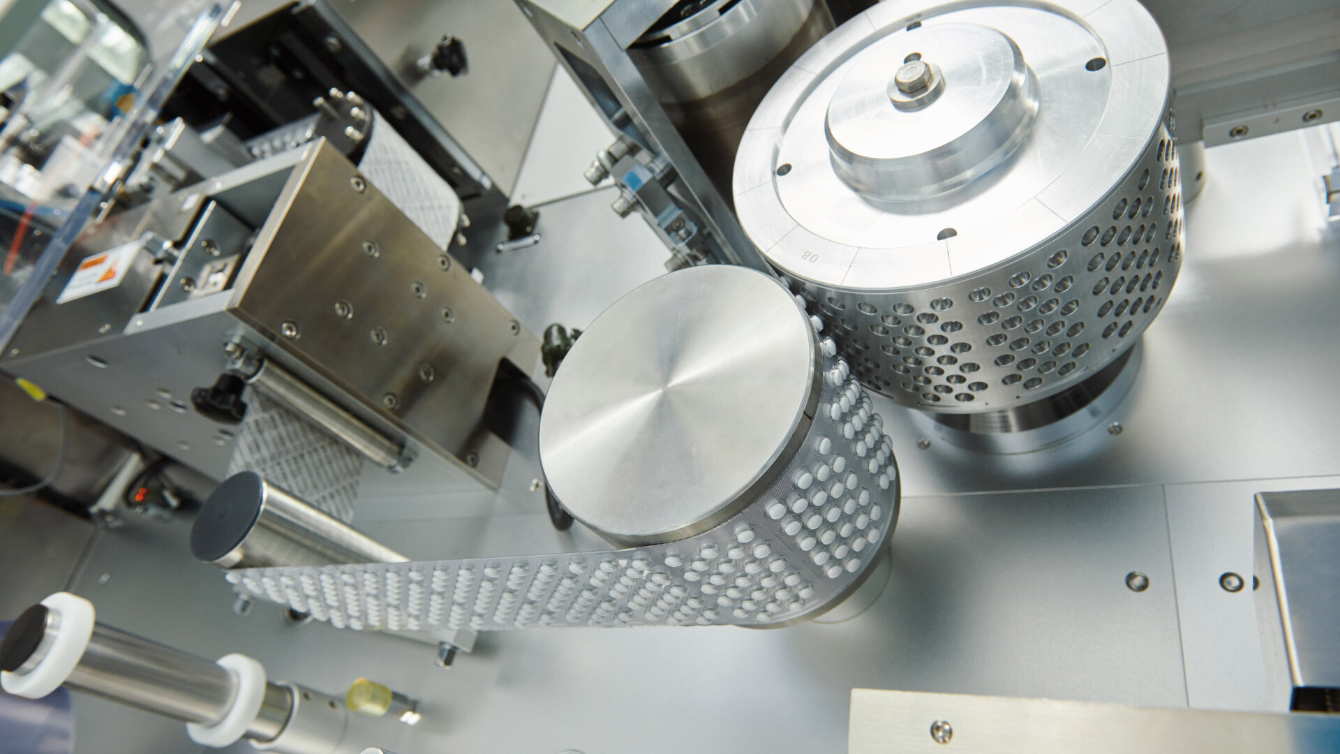 Detailansicht eines automatisierten Tablettenherstellungsprozesses in einem pharmazeutischen Produktionslabor. Die hochwertige Edelstahlmechanik und die pr&auml;zisen Walzsysteme gew&auml;hrleisten kontrollierte, GMP-konforme Fertigung und h&ouml;chste Qualit&auml;tssicherung. Optimale Umgebung f&uuml;r pharmazeutische Analytik und zuverl&auml;ssige Produktfreigabe.