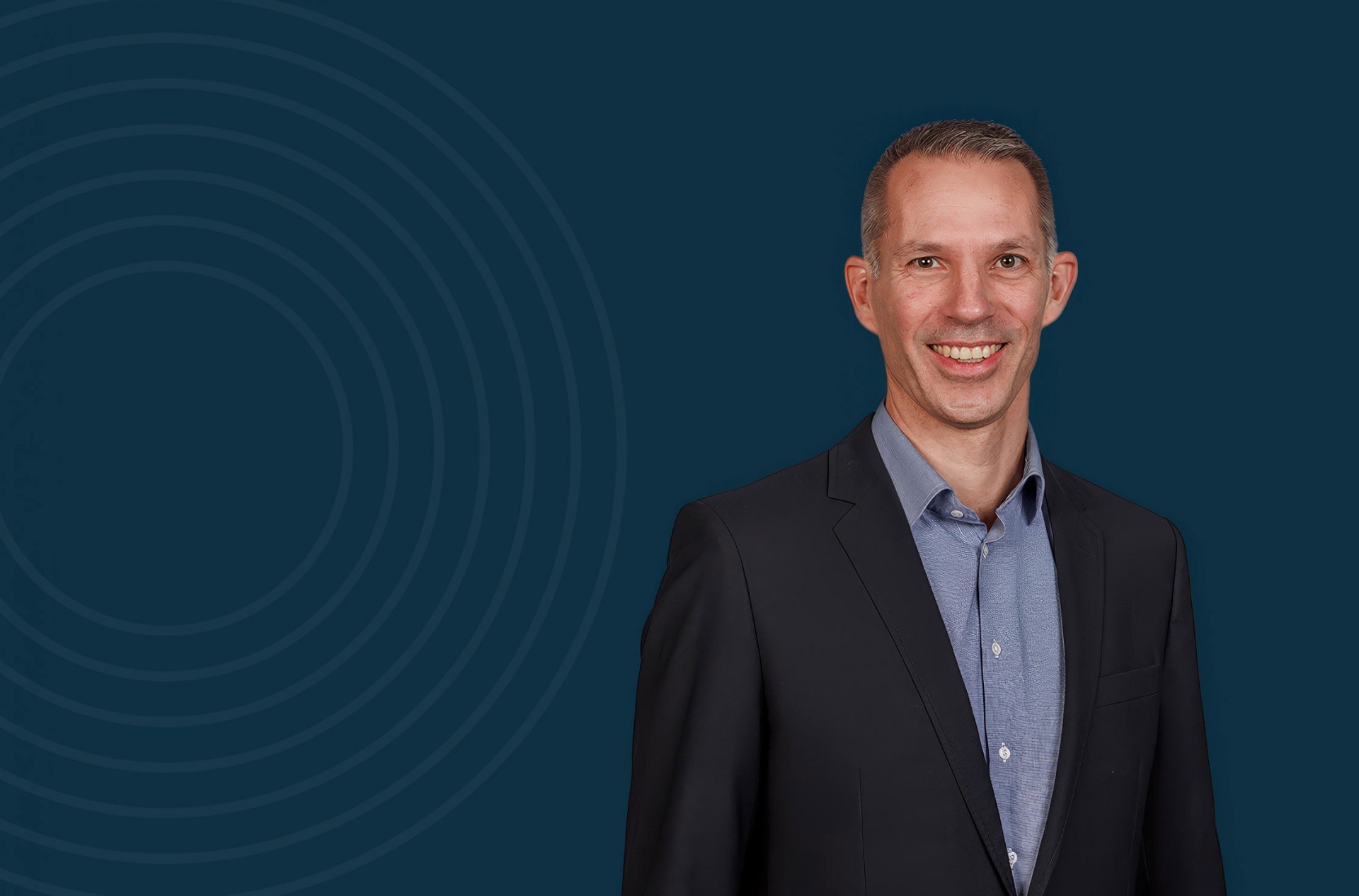 Ein professionelles Portr&auml;t eines Gesch&auml;ftsmannes in dunklem Anzug und hellblauem Hemd vor einem einfarbigen, dunkelblauen Hintergrund mit dezenten konzentrischen Kreisen. Das Bild vermittelt Seriosit&auml;t und Vertrauensw&uuml;rdigkeit &ndash; ideal f&uuml;r B2B-Kommunikation in regulierten Branchen und Unternehmensdarstellungen.